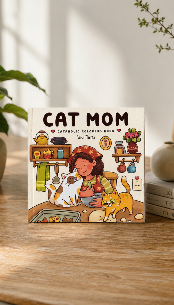 A children's coloring book titled "CAT MOM" by Vivi Tertia sits on a wooden table in a softly styled indoor setting. The cover features a colorful illustration of a woman with a cat and a kitten in a cozy kitchen scene.