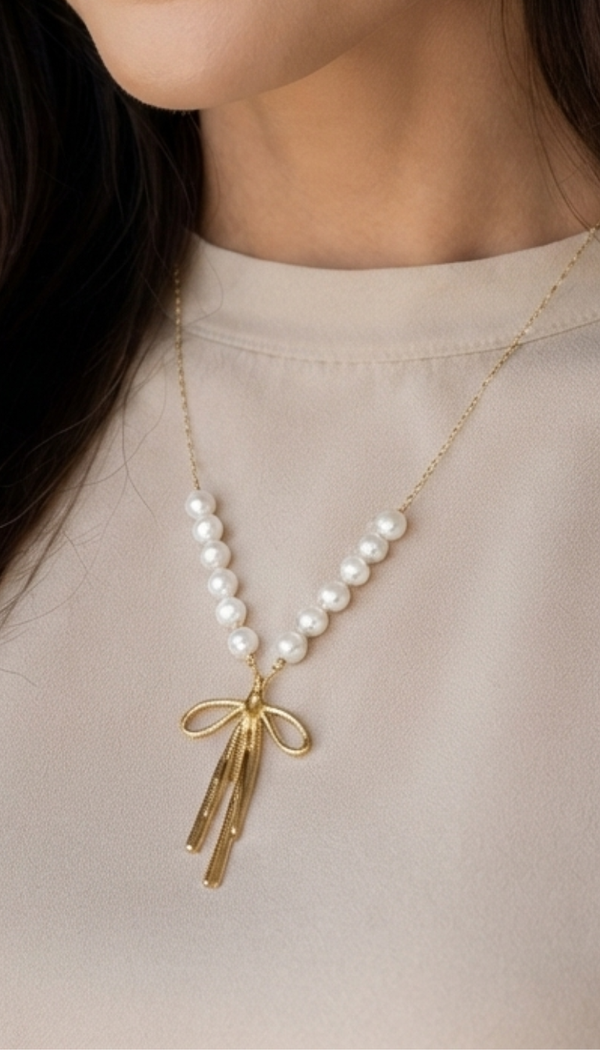 "A close-up shot of a woman wearing an elegant gold stainless steel necklace, featuring a double strand of luminous white pearls that gather into a polished gold bow pendant with a radiant sparkle."