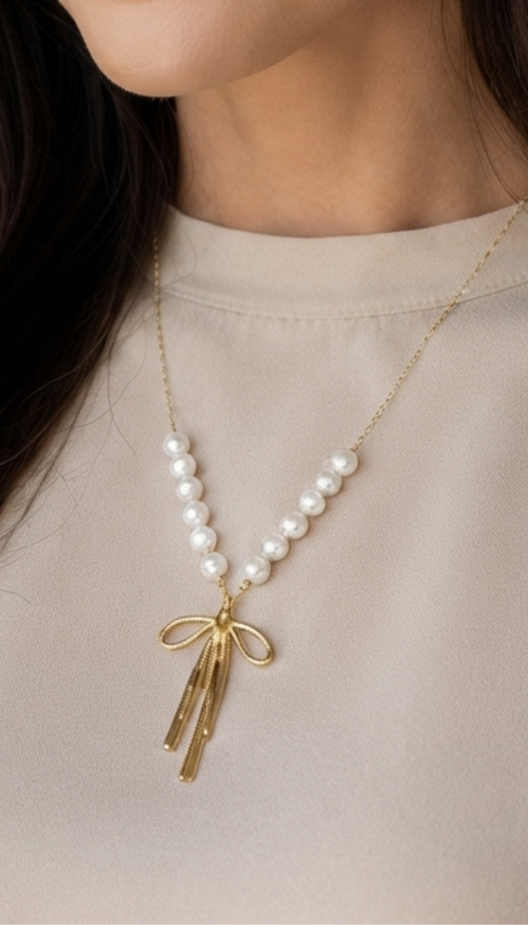 "A close-up shot of a woman wearing an elegant gold stainless steel necklace, featuring a double strand of luminous white pearls that gather into a polished gold bow pendant with a radiant sparkle."